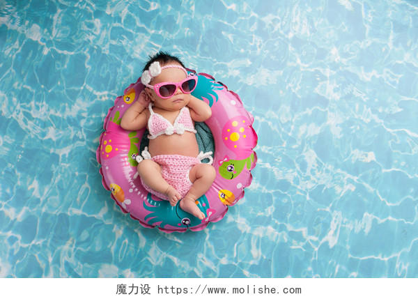 蓝色泳池里穿着粉色比基尼带着粉色太阳镜躺在充气游泳圈里的小女孩婴儿亲子游泳